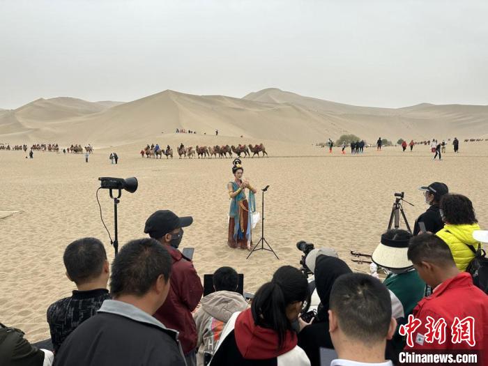圖為2023年4月底，敦煌大漠“逐舞者”奧楠在鳴沙山月牙泉景區(qū)視頻直播，吸引游人圍觀?！●T志軍 攝